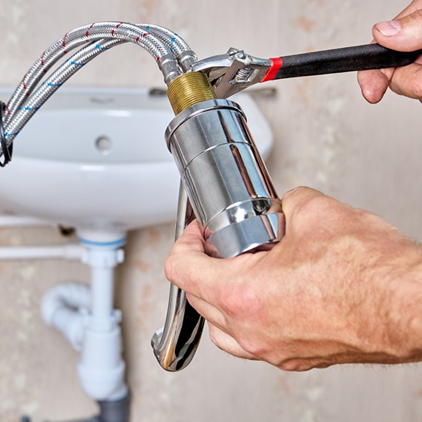 Licensed plumber fixing a bathroom sink faucet with a wrench in a residential property in Ottawa, ON