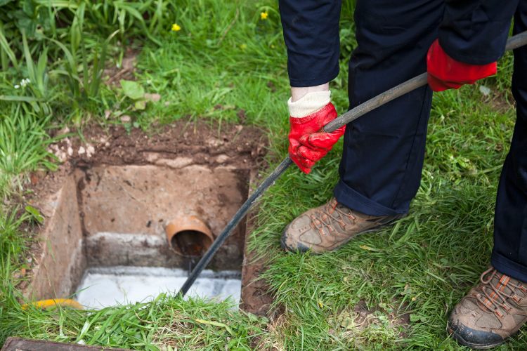 Technician clearing a blocked outdoor drain inspection chamber