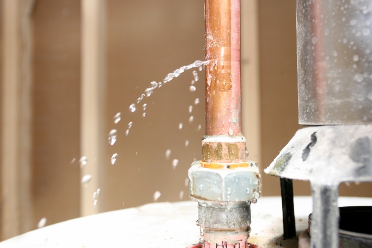 Close-up of copper pipe with water spraying from leaking joint connection