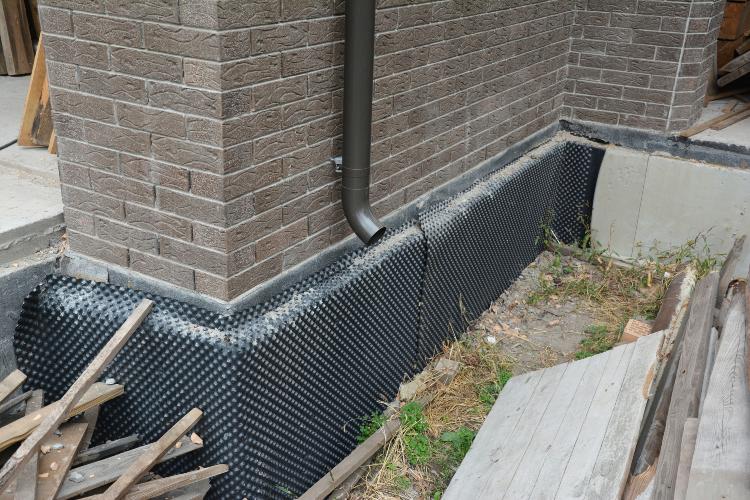 Exterior house foundation with downspout and waterproofing membrane for drainage protection