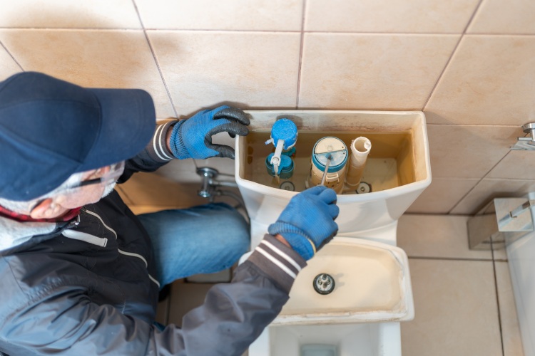 Plumber repairing a toilet tank and adjusting internal flush components